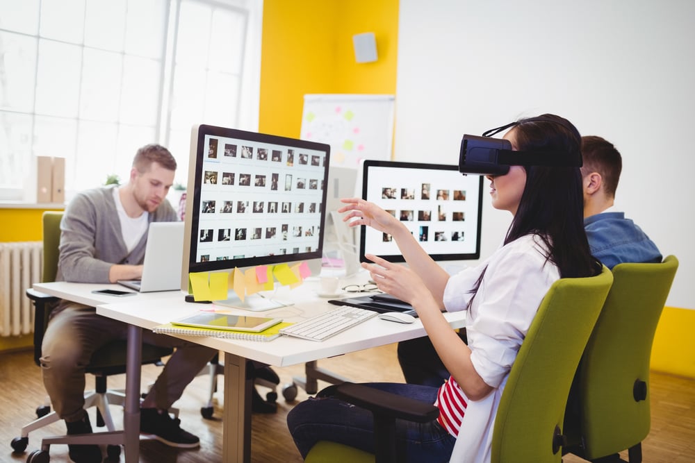 Yoiung female executive enjoying augmented reality headset with colleagues sitting at creative office